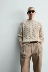 Sweater de punto con diseño de trenzas, color beige, cuello redondo y manga larga con terminaciones en rib.