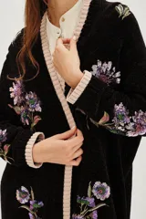 Cardigan negro de punto con bordados florales y aplicaciones de lentejuelas. Presenta terminaciones en tejido acanalado de color beige en los puños, el ruedo y a lo largo de la apertura frontal.