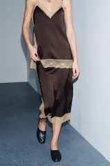 Top de tejido satinado color marrón oscuro, con escote recto y tirantes finos ajustables. Presenta aplicación de encaje color beige a contraste en el escote y el bajo.