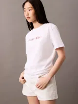 Remera blanca de manga corta con cuello redondo y corte regular. Presenta el logo de Calvin Klein estampado en el pecho con un efecto degradado de colores que va del rosado al cobre.