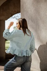 Camisa de algodón a rayas verticales en color verde y blanco, con cuello camisero, mangas largas y un detalle de volado en el ruedo que le otorga una silueta acampanada.