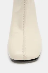 Botín de cuero color crema con puntera cuadrada y cierre de cremallera en la parte trasera. El tacón es ancho y de color negro. La altura del tacón es de 8,5 cm.