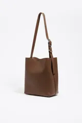 Bolso de hombro Bimba y Lola modelo Carlino, de estructura rígida y tamaño mediano, confeccionado en piel vacuna color tostado. Presenta asa regulable de piel con hebilla metálica y logo impreso en la parte inferior.