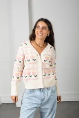 Cárdigan de punto color crema con diseño de flores en tonos rosados y verdes, guardas caladas, escote en V, cierre frontal con botones y terminaciones acanaladas.