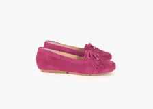 Mocasines de cuero gamuzado color uva (fucsia oscuro), con flecos en la capellada y un lazo frontal con herrajes metálicos dorados. El interior está forrado en cuero y la suela es de goma flexible.