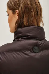 Chaleco acolchado de corte corto, color verde oliva, con cuello alto ajustable mediante cordones elásticos y cierre frontal con cremallera.