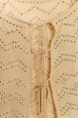 Top color beige con escote cuadrado y tirantes finos. Diseño con tachuelas combinadas a tono y cierre en la espalda con lazadas.