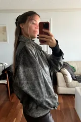 Campera bomber de cuero ovino con efecto desgastado en tonos grisáceos y negros. Presenta cuello camisero, cierre frontal con broches forrados y diseño holgado.