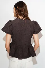 Top color marrón oscuro con textura en relieve, cuello redondo, mangas cortas abullonadas y bajo en evasé con volantes. Cierre en la espalda con botones.