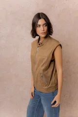 Chaleco de gamuza color marrón con acabado aterciopelado, cuello alto con broche a presión, cierre frontal metálico y bolsillos laterales con cierre.
