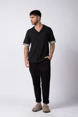 Camisa de punto de manga corta con cuello tipo bowling y cierre frontal de botones. Presenta un diseño texturizado con franjas verticales y detalles de contraste en blanco en los bordes de las mangas.