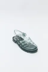 Sandalias jelly color gris translúcido, con diseño entrecruzado y hebilla lateral ajustable.