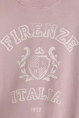 Buzo de tejido de punto color rosado pálido, con cuello redondo, hombros caídos y puños y bajo acanalados. Presenta un estampado frontal en blanco con el texto "Firenze Italia" y un escudo central con el año "1932".