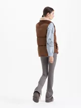 Chaleco matelaseado color marrón camel con canesú en corderoy color chocolate. Presenta cuello con corderito, cierre frontal con botones a presión, bolsillos con tapa y un parche bordado en el bolsillo derecho.