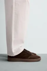 Zapatilla de estilo urbano confeccionada en piel con acabado de serraje en color marrón. Presenta cierre mediante cordones al tono, detalle de pespuntes en el empeine y suela de goma a tono.