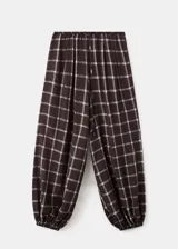 Pantalón balloon de tiro medio en color marrón oscuro con estampa de cuadros. Cuenta con cintura ajustable con goma y cierre de lazo, además de dos bolsillos laterales y diseño abuchonado en los tobillos.