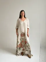 Vestido largo beige con diseño holgado, escote en V y mangas largas, adornado con un gran estampado floral en tonos marrones y verdes en la parte inferior.