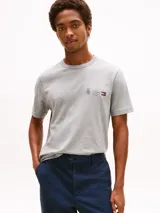 Remera de cuello redondo y manga corta en color gris melange. Presenta un pequeño logo bordado en el pecho que combina un escudo, el nombre de la marca y la bandera característica de Tommy Hilfiger.
