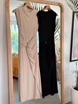 Vestido largo color beige, sin mangas, con escote redondo y detalle de frunces laterales en la cintura que crean un efecto drapeado y una abertura frontal en la falda.