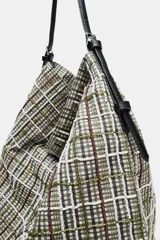 Bolso tipo shopper de tejido con diseño de cuadros en tonos verdes, blancos y marrones, decorado con apliques brillantes. Cuenta con asa de hombro ajustable en material sintético negro, cierre mediante botón imantado y bolsillo interior con cremallera.