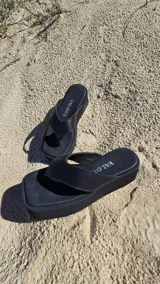 Ojotas de cuero negro con plataforma corrida, tira ancha tipo dedo y plantilla acolchada.