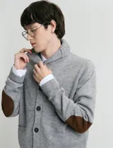 Cardigan de punto color marrón con cuello esmoquin, cierre frontal con botones y presilla superior. Presenta mangas largas con coderas en contraste y bolsillos frontales de ribete.