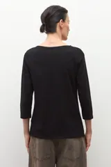 Remera negra de manga tres cuartos con escote bote y un lazo o bufanda del mismo material anudado al cuello.