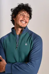 Buzo de cuello alto con cierre frontal parcial, diseño bicolor con cuerpo en verde y mangas raglán en azul. Presenta el logo de la marca bordado en el pecho.