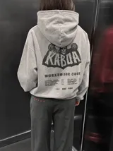 Canguro de felpa gris melange con capucha, manga larga y estampa trasera de estilo rockero con tipografía y calavera.