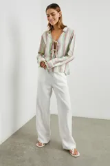 Blusa de lino a rayas verticales de color blanco, naranja, verde y marrón, con cuello camisero, mangas largas con puños y lazos ajustables en el escote.