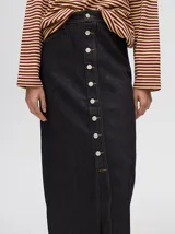 Pollera midi de denim color marrón, de tiro medio y corte recto. Presenta cierre frontal con botones metálicos a la vista y un tajo central en el ruedo con terminación deshilachada.