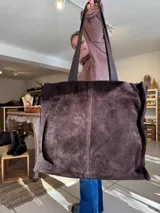 Cartera tipo tote de gamuza color chocolate, con costura central vertical y doble asa de hombro. Incluye bolsillo frontal y cierre superior.