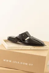 Sandalias tipo mule de cuero negro, con diseño de puntera cuadrada, aberturas laterales y detalle de remaches metálicos decorativos.