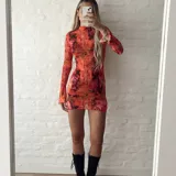 Vestido corto de microtul elastizado con estampado floral en tonos naranja, rosa y negro. Tiene cuello alto y mangas largas acampanadas.