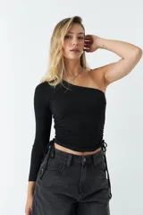 Top asimétrico de una sola manga larga, color azul, con jaretas ajustables en ambos laterales del torso que permiten regular el largo de la prenda.