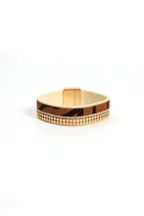 Brazalete ancho con estampado animal print y detalles de cadenas doradas y strass. Cierre magnético.