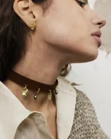 Gargantilla tipo choker de gamuza con dijes colgantes artesanales de metal y perlas naturales. Cuenta con tiras largas para atar y ajustar en la parte posterior.