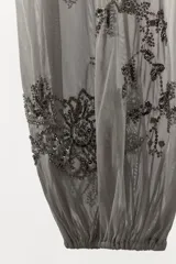 Pantalón de tiro medio confeccionado en tejido de tul transparente con forro interior corto. Presenta bordados florales con aplicaciones de lentejuelas, cintura elástica y bajo abullonado con acabado elástico.