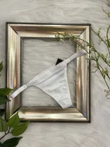 Tanga de lycra color blanco con detalle de puntilla en los bordes y tiras laterales regulables.