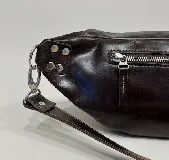Riñonera de cuero color negro, con múltiples compartimentos con cierre metálico, detalles de tachas en los laterales y correa regulable.