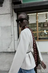 Blazer de textura suave, cuello redondo y manga larga. Presenta un diseño minimalista con cierre frontal mediante un cinturón fino de cuero con hebilla metálica.