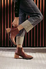 Botín de cuero negro, caña corta, con punta cuadrada y cierre lateral. Presenta un tacón de madera de altura media y detalles en charol con textura de cocodrilo en el talón.