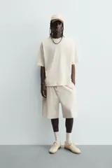 Bermuda de corte relajado, color crema o blanco roto, con textura acanalada (canalé). Presenta cintura elástica ajustable con cordón, bolsillos de vivo frontales y un bolsillo plastrón trasero.