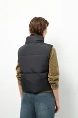 Chaleco puffer color beige, sin mangas, con cuello alto y cierre frontal con cremallera.