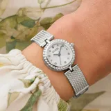Reloj analógico Guess modelo Holly con caja redonda de 23mm y correa tipo brazalete de acero inoxidable en tono plateado. La esfera presenta un acabado radiante con índices de cristales y bisel decorado con textura de cuentas.