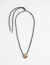 Collar con cordón negro y dije circular dorado con textura irregular.