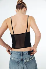 Corsé de escote en pico con tirantes finos, confeccionado en una combinación de tejido opaco y paneles de tul transparente, con costuras visibles a tono.