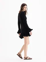 Vestido corto de punto celeste, con silueta ajustada, cuello medio alto y mangas largas. Cuenta con volados plisados en los puños y en el ruedo.