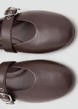 Zapato plano estilo Mary Jane color marrón, confeccionado en piel de ovino, con punta fina y tira en el empeine con hebilla metálica plateada.