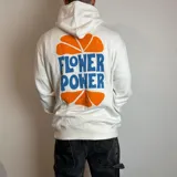 Canguro blanco con capucha, de corte regular, con estampado gráfico en la espalda que incluye la frase 'Flower Power' en letras azules y detalles de pétalos naranjas.